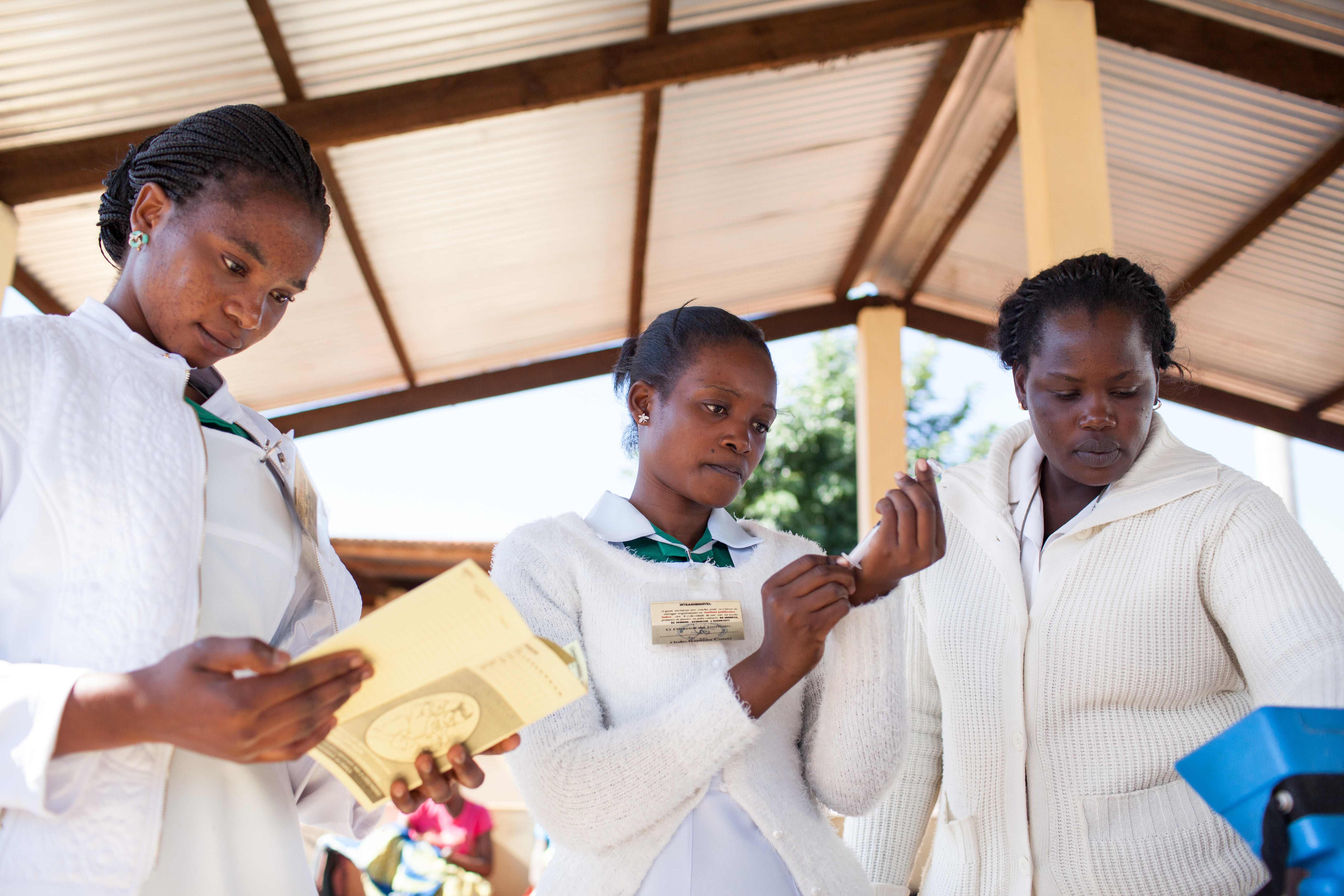 Three female doctors stand around a table at a clinic preparing injections