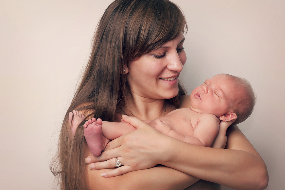 A mother cradles a naked newborn baby and smiles down lovingly at the infant.