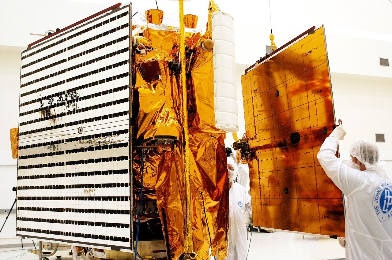 Technicians in a workshop fitting a solar panel to a satellite.