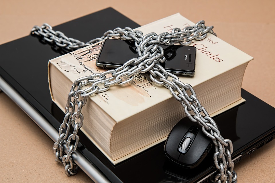 A laptop, book and phone sit on a desk, wrapped in chains.