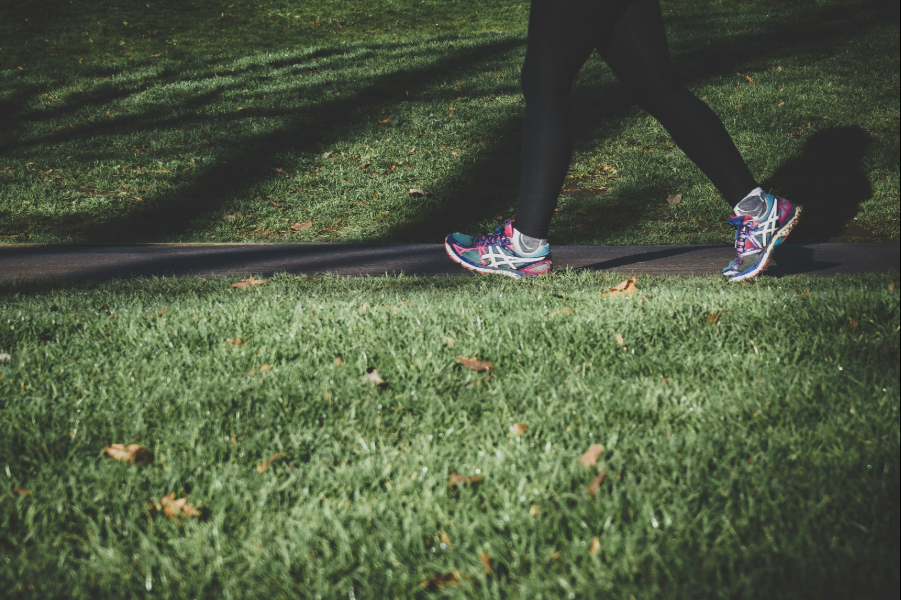 Person exercising Person walking on a path in a grassy area with colorful running shoes.