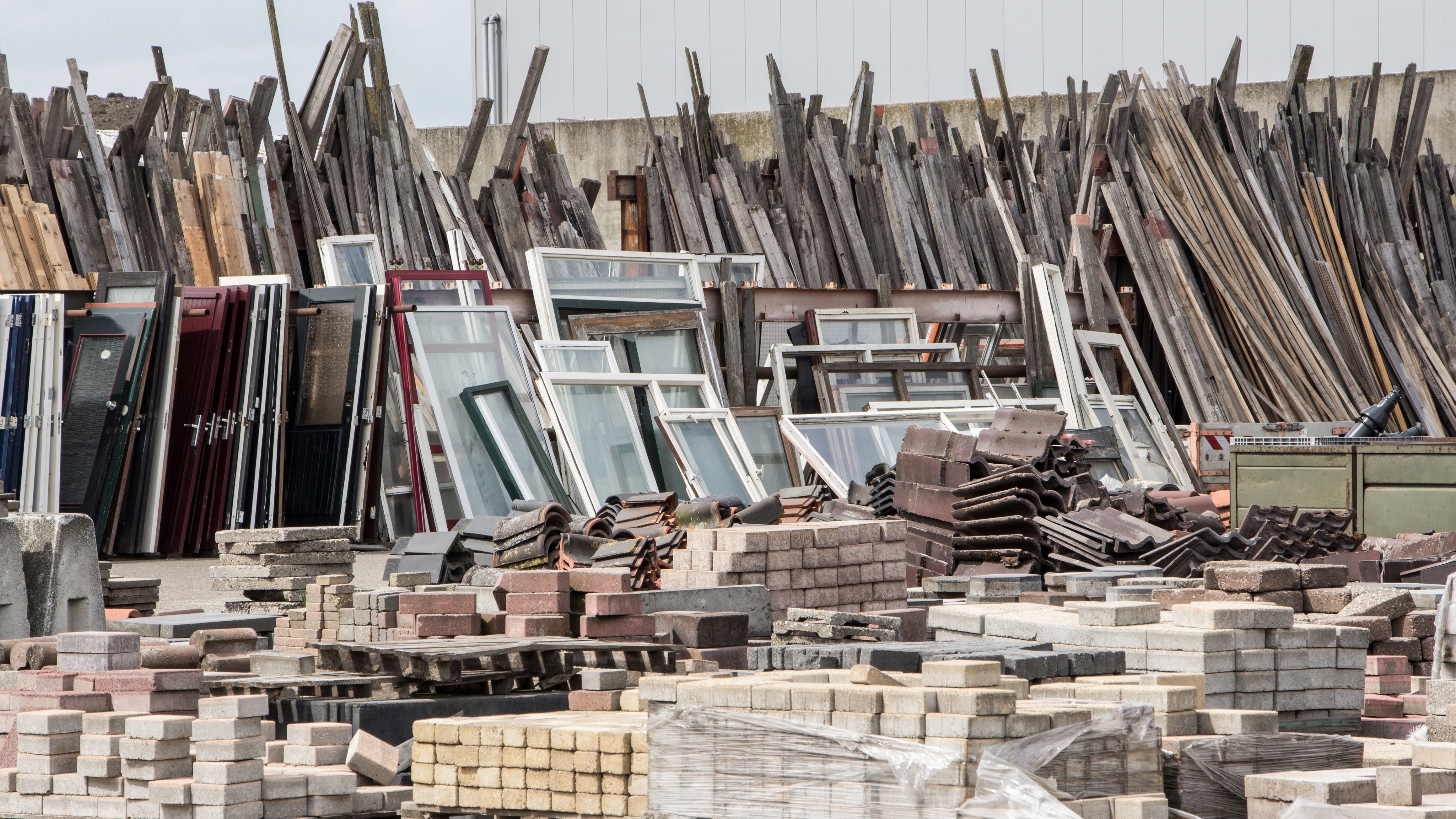 Piles of construction resources. including windows and frames, various timber, bricks and roofing materials. Symbolises the resource heavy nature of construction.