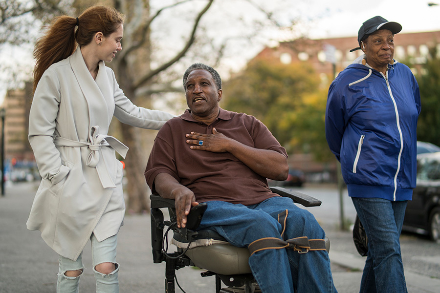 White teenager girl talking with disabled wheel-chaired African American man and woman when they walking on the street in Bronx, New York, together