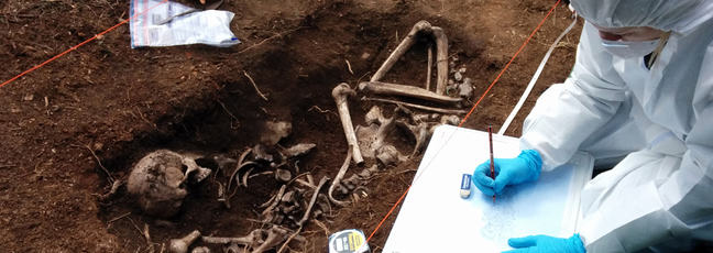 A forensic scientist examines human remains in an open grave, in order to identify the dead
