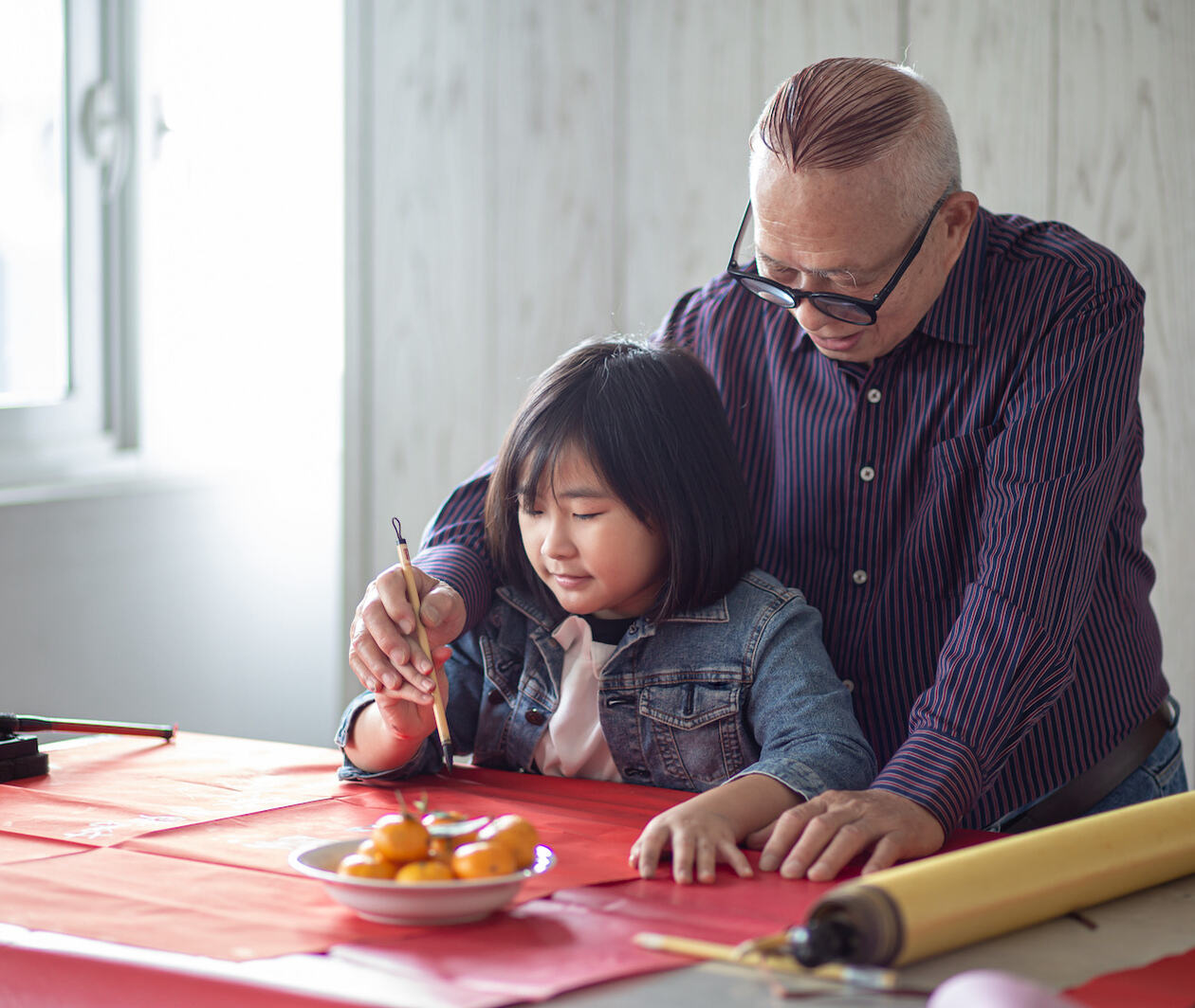 Elderly Chinese man practicing calligraphy with his grand-daughter