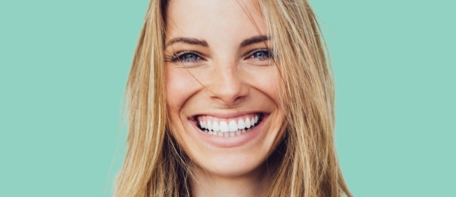 A woman with blonde hair grins in front of a green background.