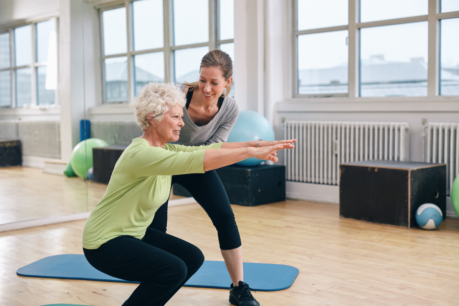 trainer helping older client squat