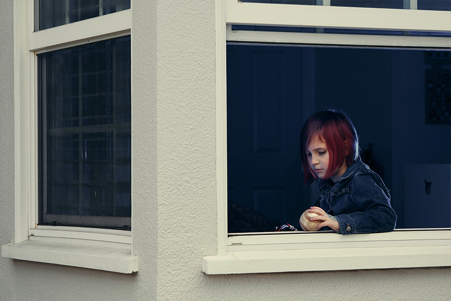 Young girl looking out of a window holding a baseball