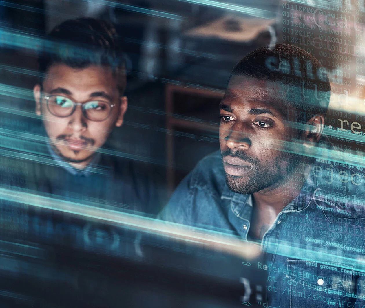 Two men gaze at a computer screen surrounded by code.