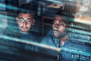 Two men gaze at a computer screen surrounded by code. 