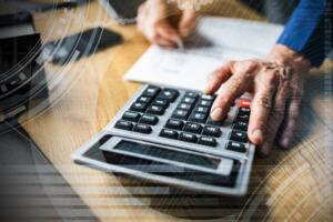 An accountant at a desk analysing a financial statement with a pen and calculator.