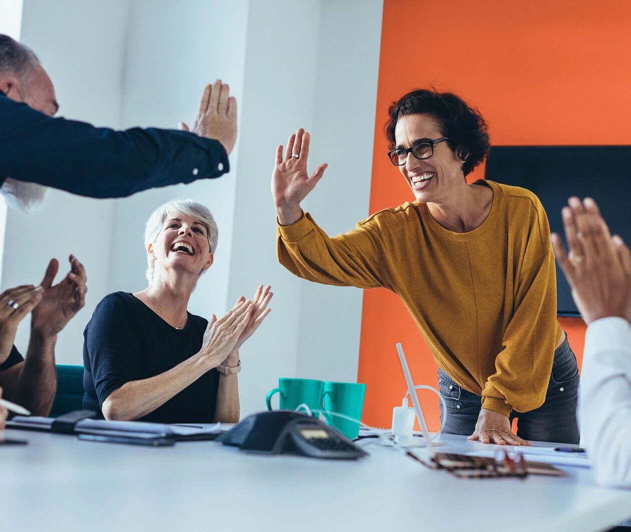 Team of men and women clapping and high-fiving around a table