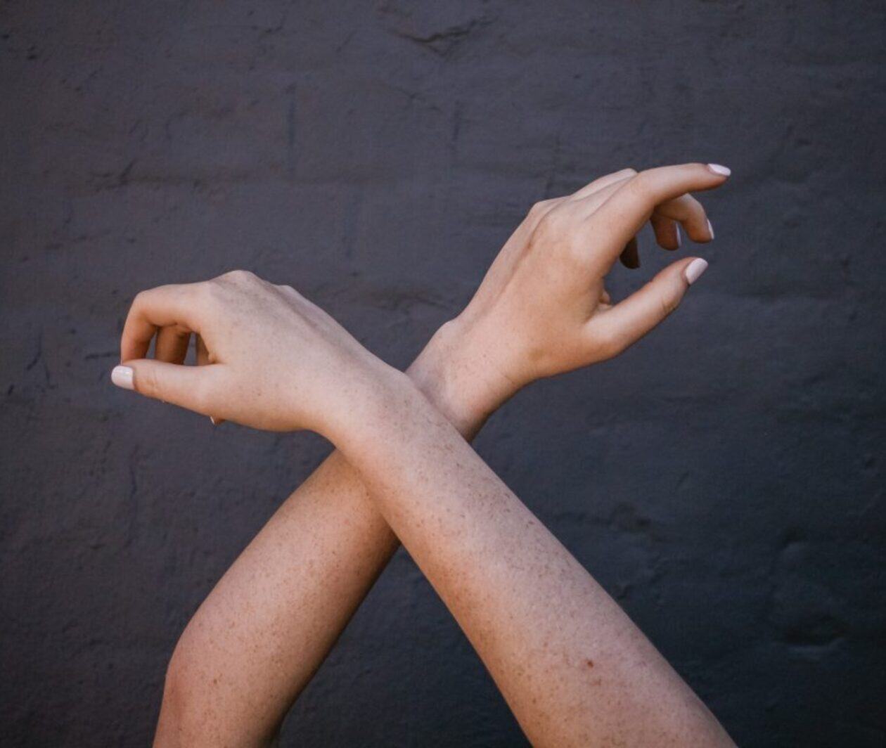 Two crossed arms and hands against a dark textured background.