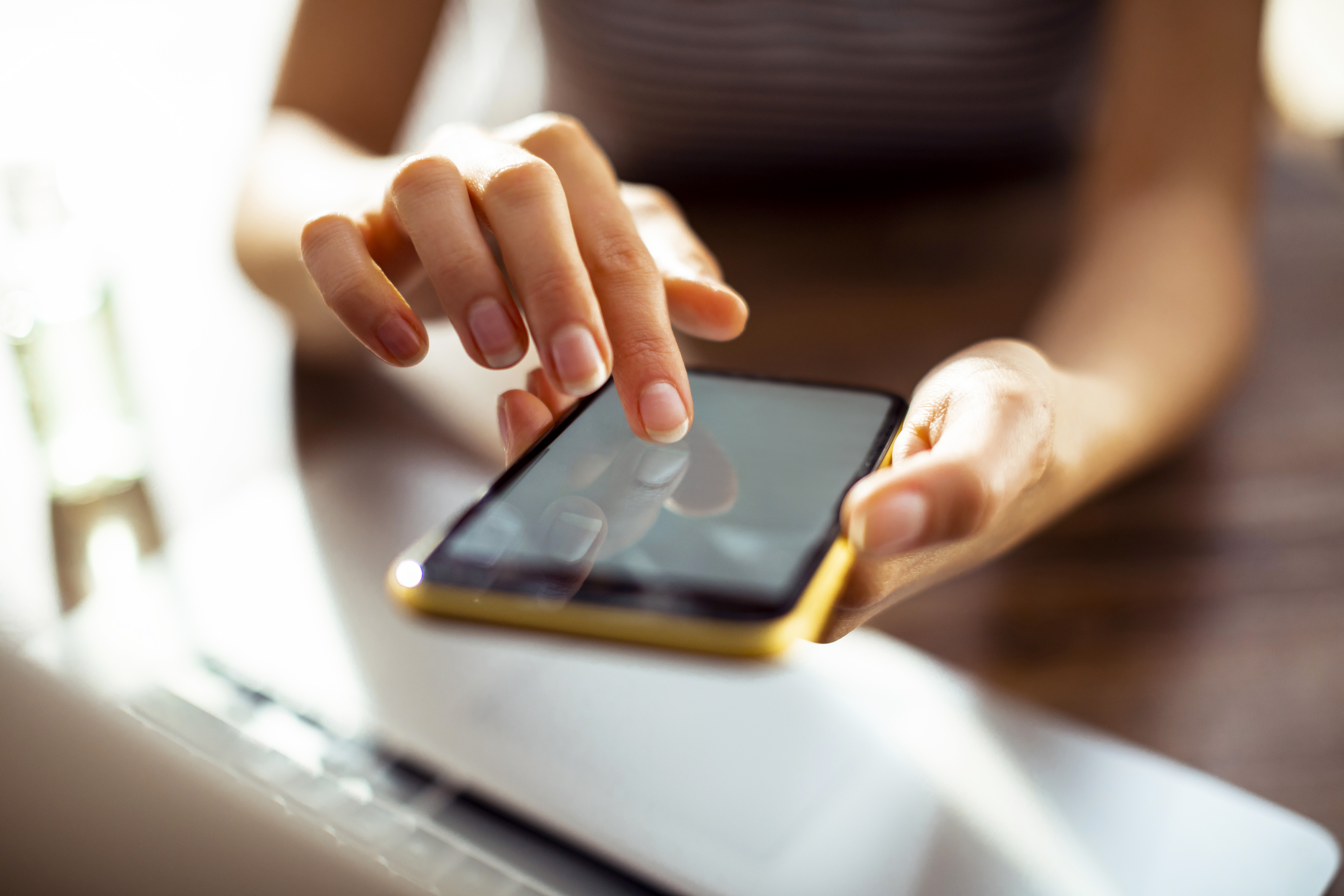 A woman scrolls on her phone whilst sat at her desk.