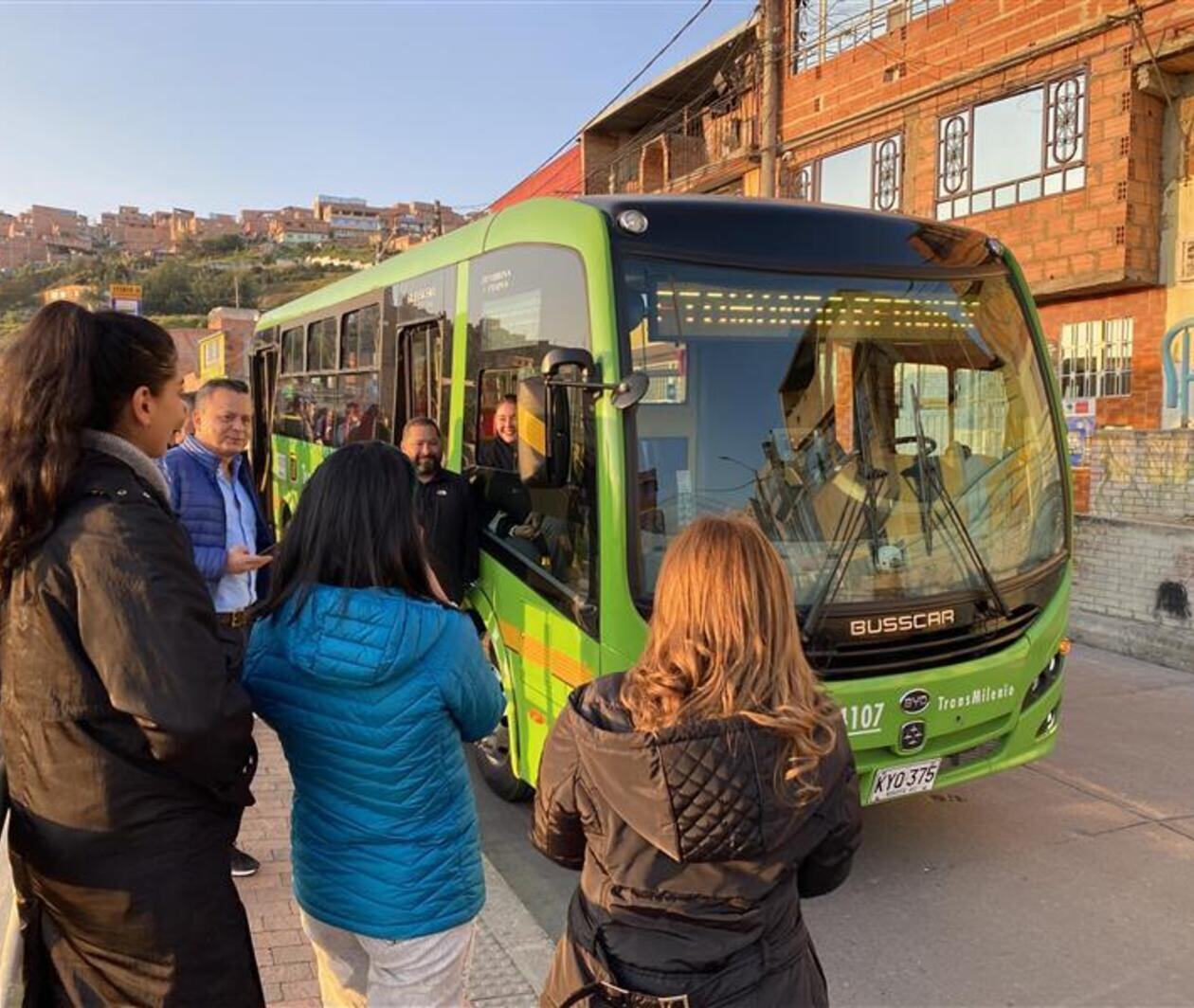 Grupo de personas hablando alrededor de un bus eléctrico verde del Transmilenio en Bogotá, Colombia.      © GIZ 