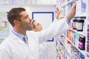 Two pharmacists reaching for medicines on a shelf.