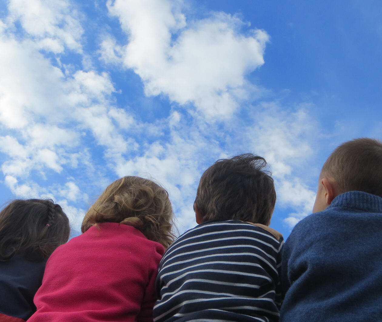 Backs of four children looking up to a blue sky with few clouds in it