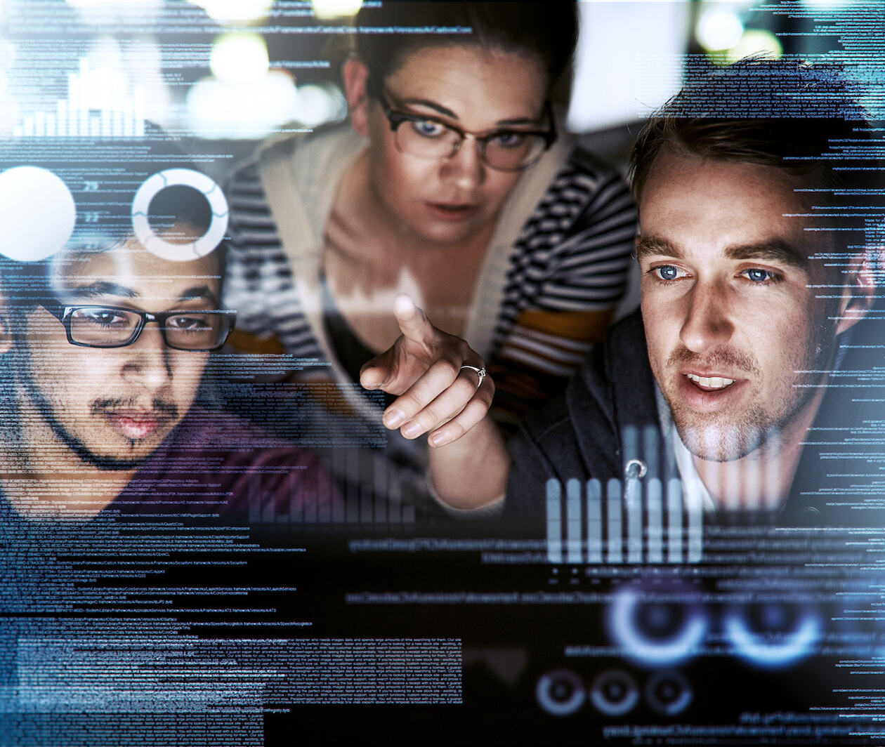 A mid-shot of three coders using a laptop superimposed over multiple lines of computer code