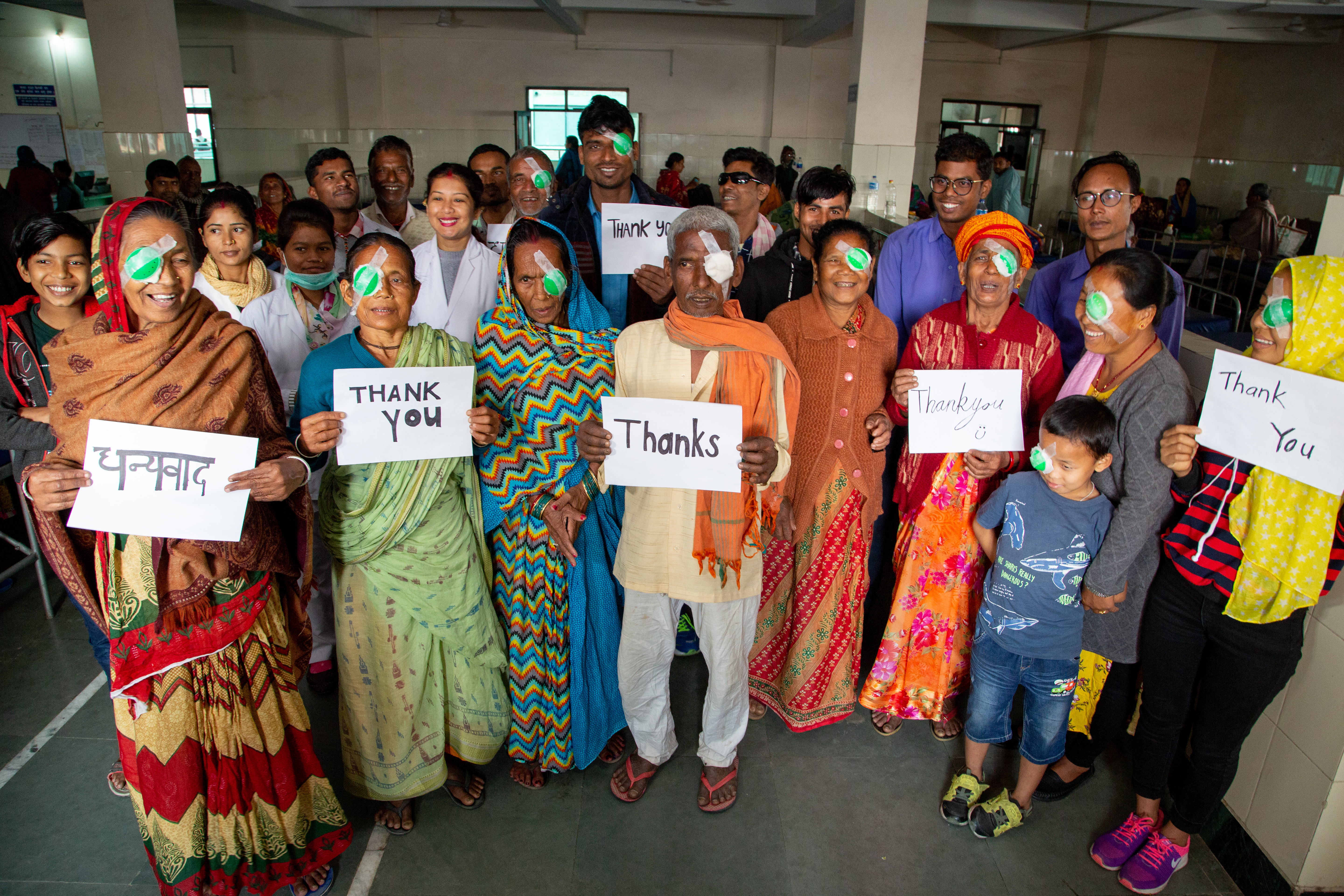 Image shows a group of patients from an eye hospital in Nepal who have just received surgery for cataract. They are holding signs saying thank you and smiling.