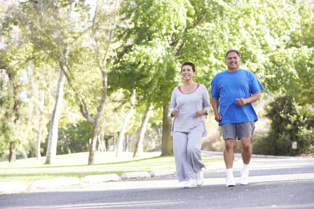 A man and woman running in a leafy park.