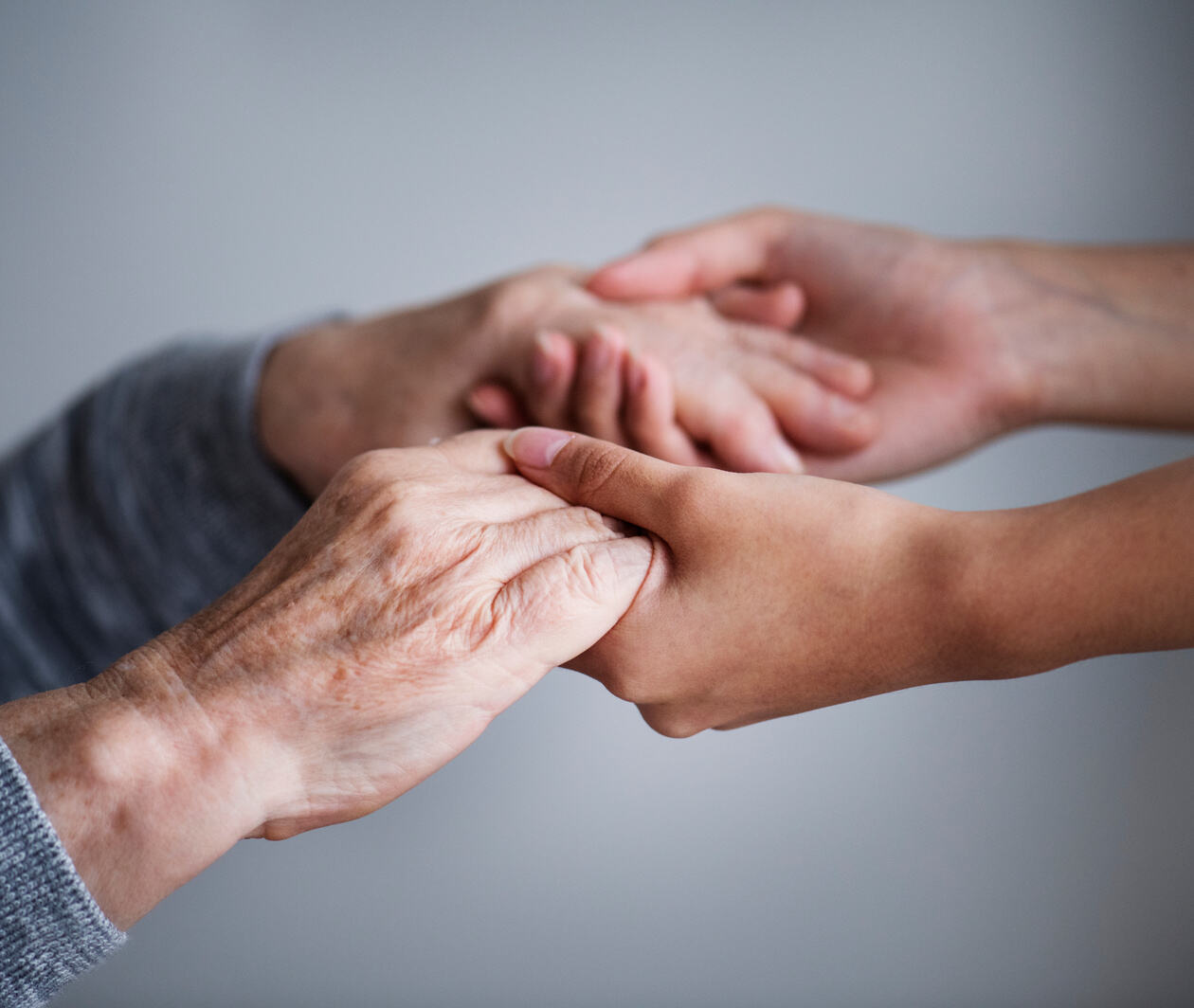 Close up of supporting hands of an elderly with Parkinson’s disease and a carer