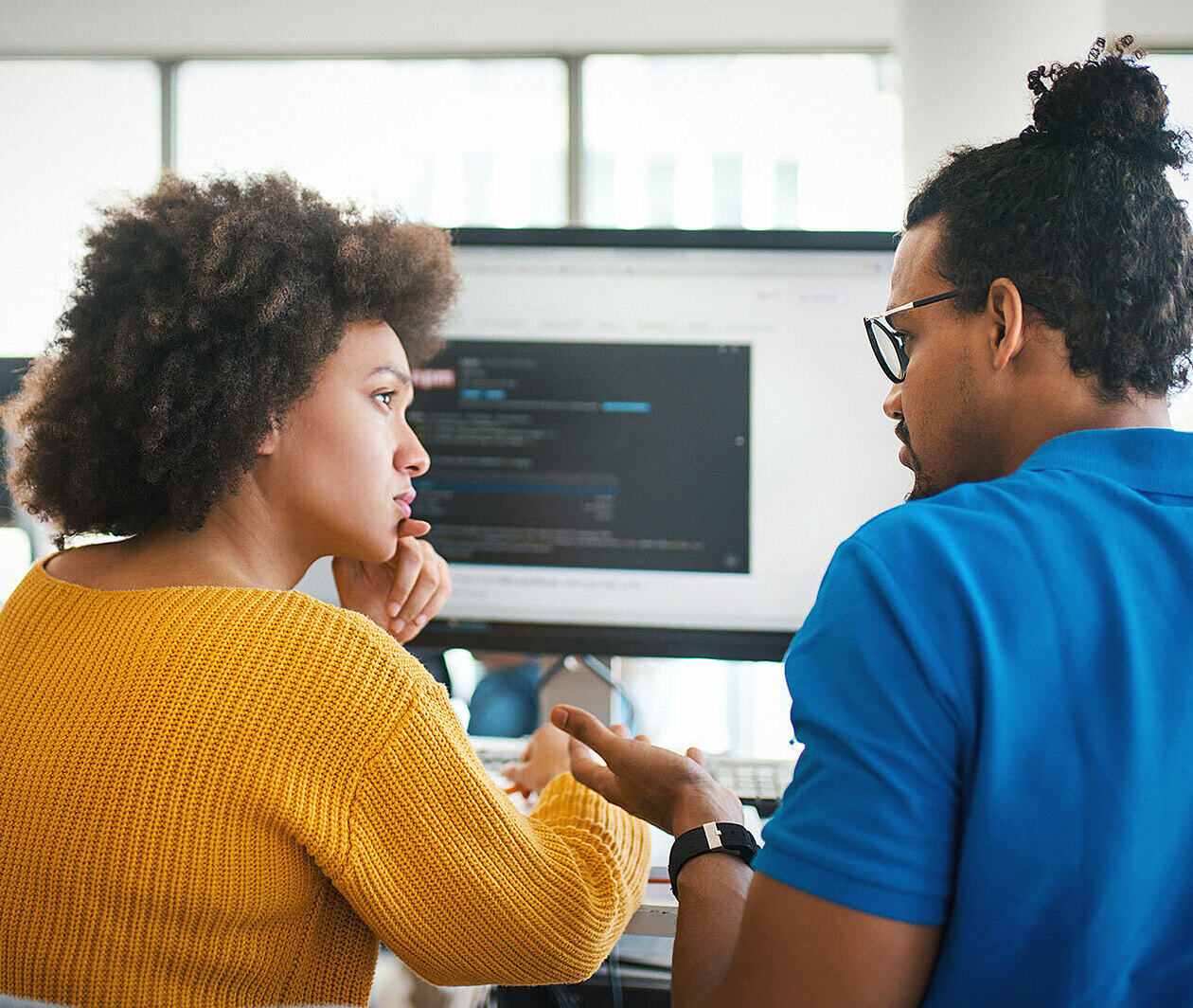 Two people working at a computer that has code on the screen.