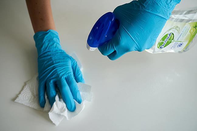 hands with gloves spraying surface and wiping with paper towel