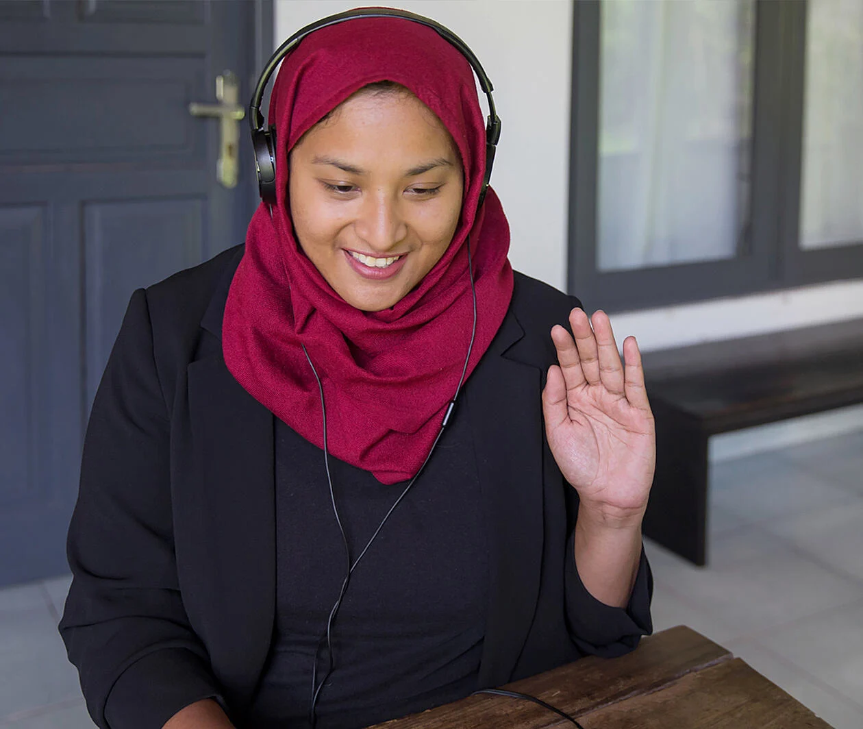 A lady with a headset on waving at a laptop