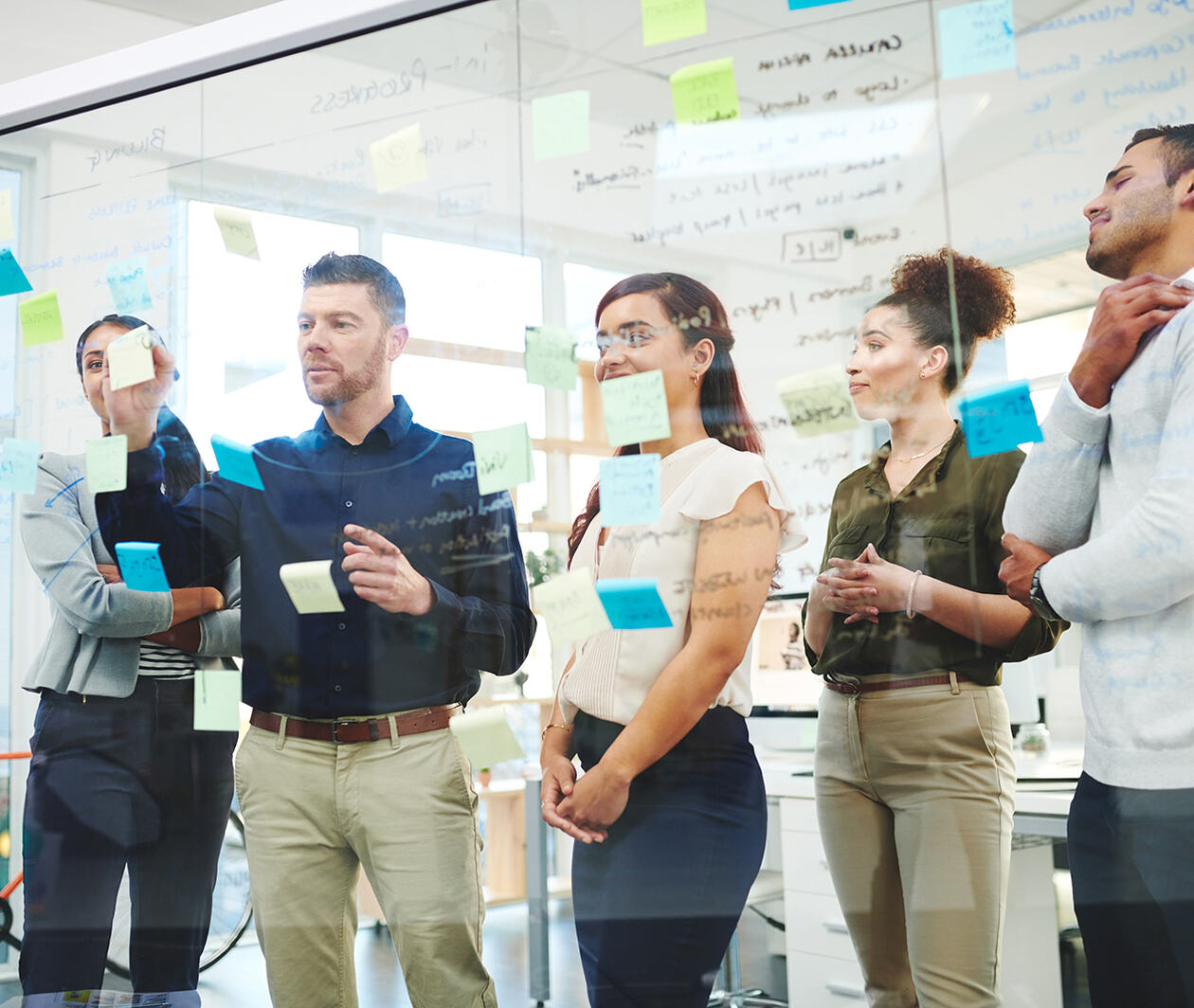 A group of business people deciding workflow with post-its on a full length glass screen