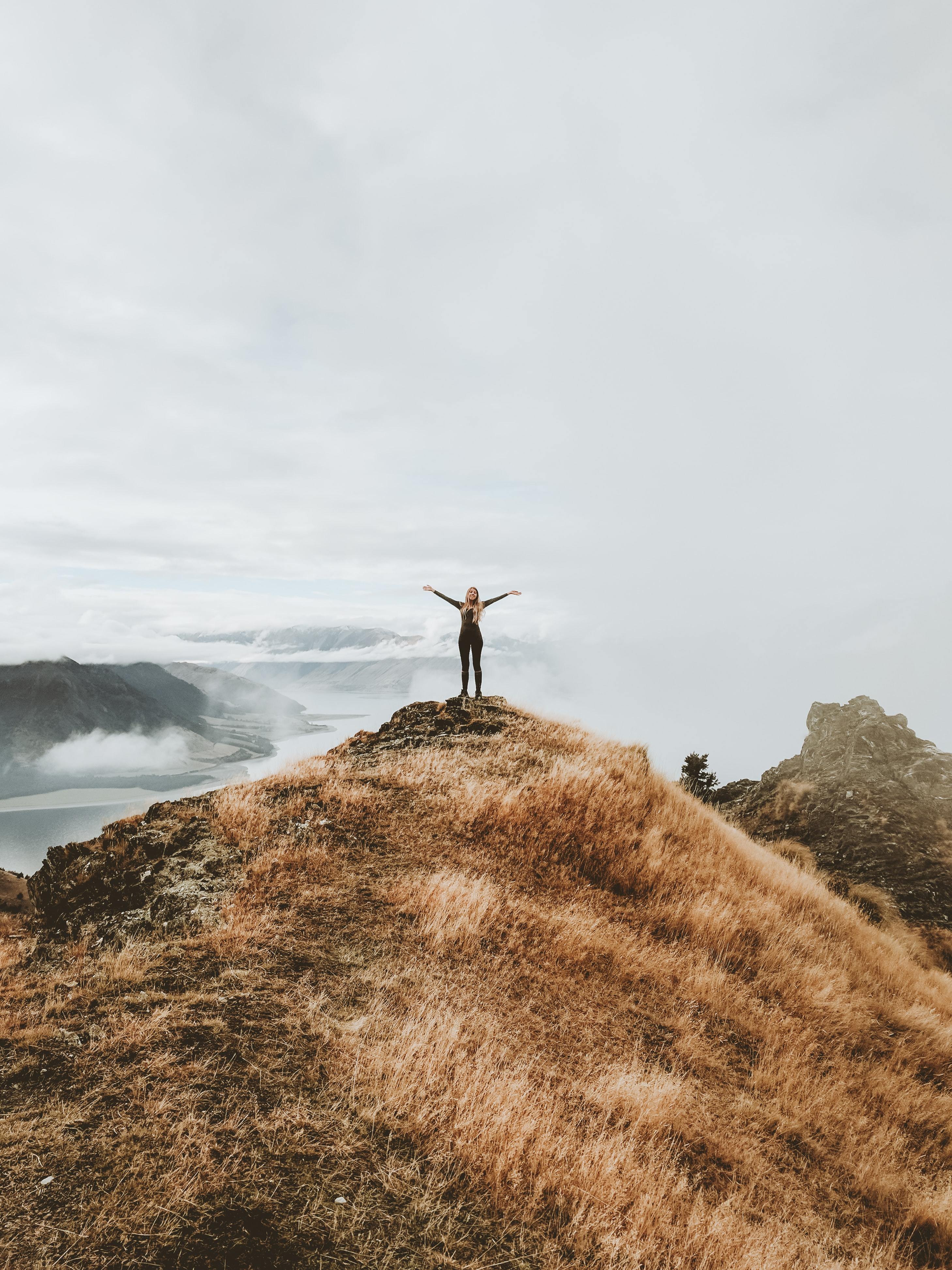 Lady standing on top of a hill reaching for the sky