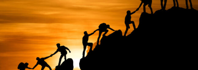 group of people on peak mountain, helping each other to the top