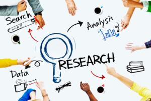 Table with Research and drawing of a magnifying glass on with different people pointing at different aspects