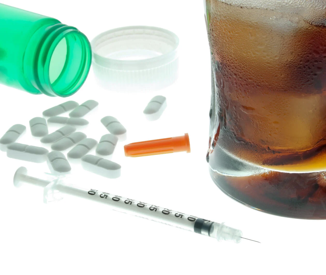 pills, a syringe and a rum and coke on a white table