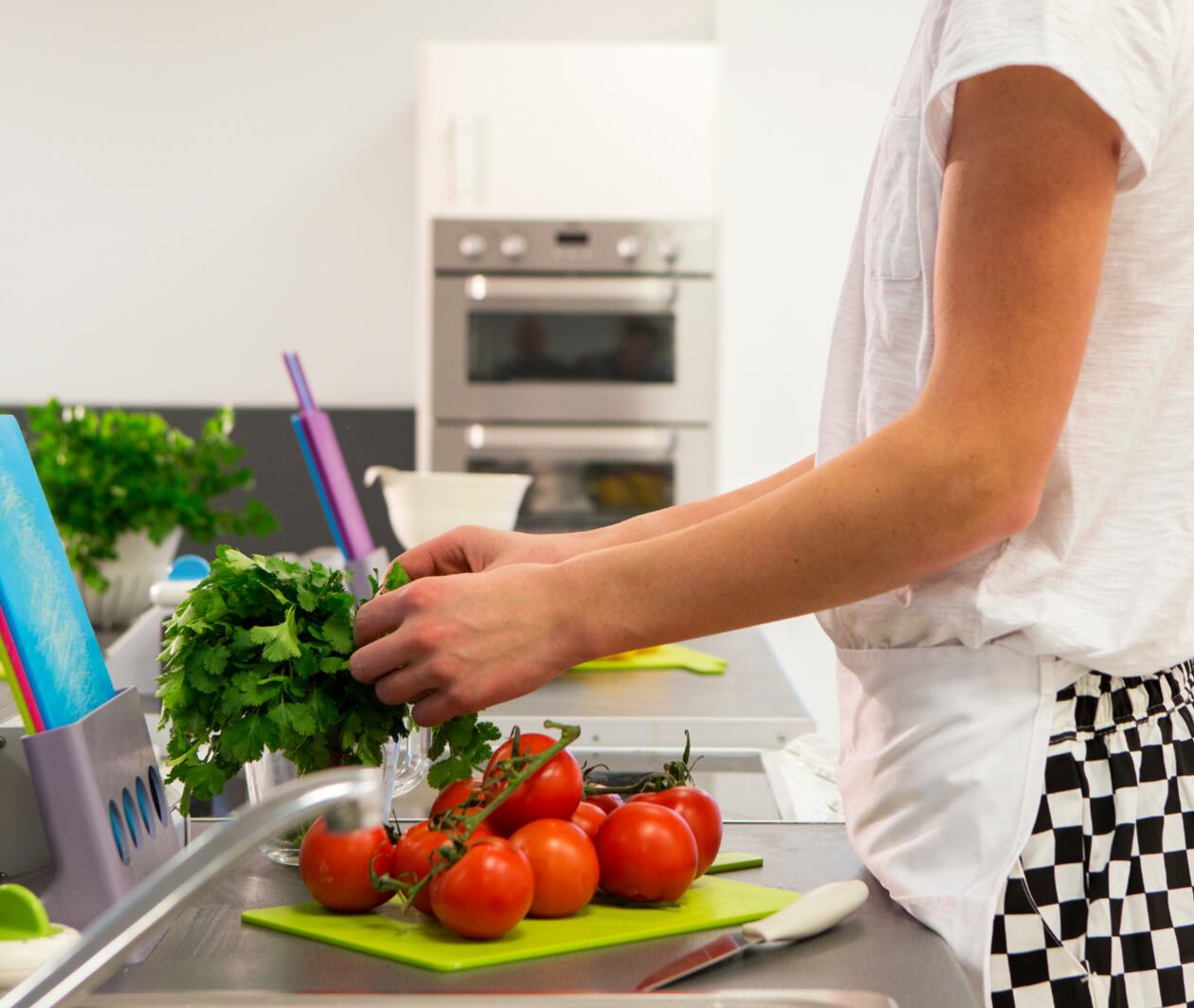 A junior chef in the kitchen wearing an apron and chopping tomatoes.