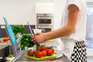 A junior chef in the kitchen wearing an apron and chopping tomatoes.