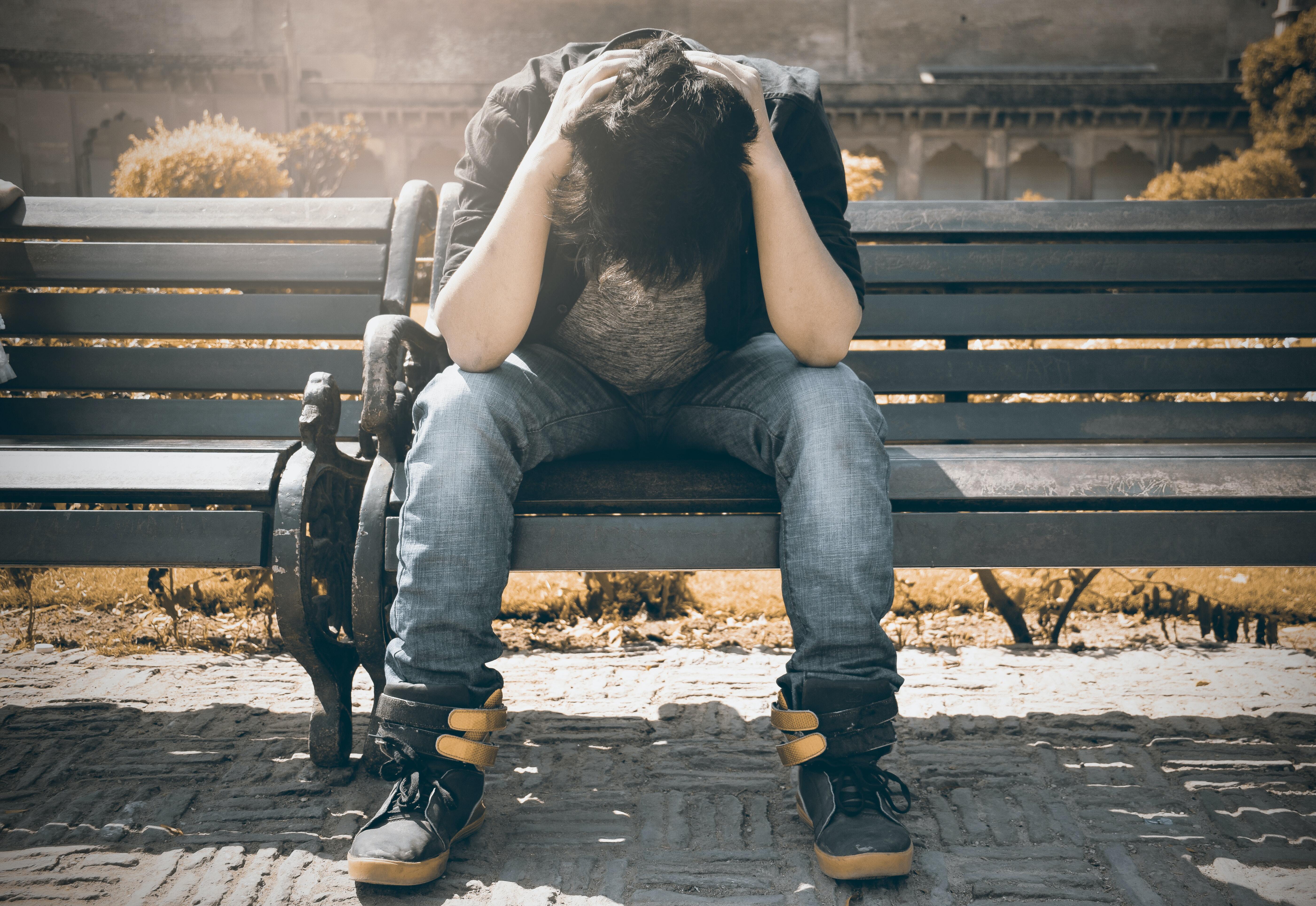 A young man sitting on a bench with his head in his hands