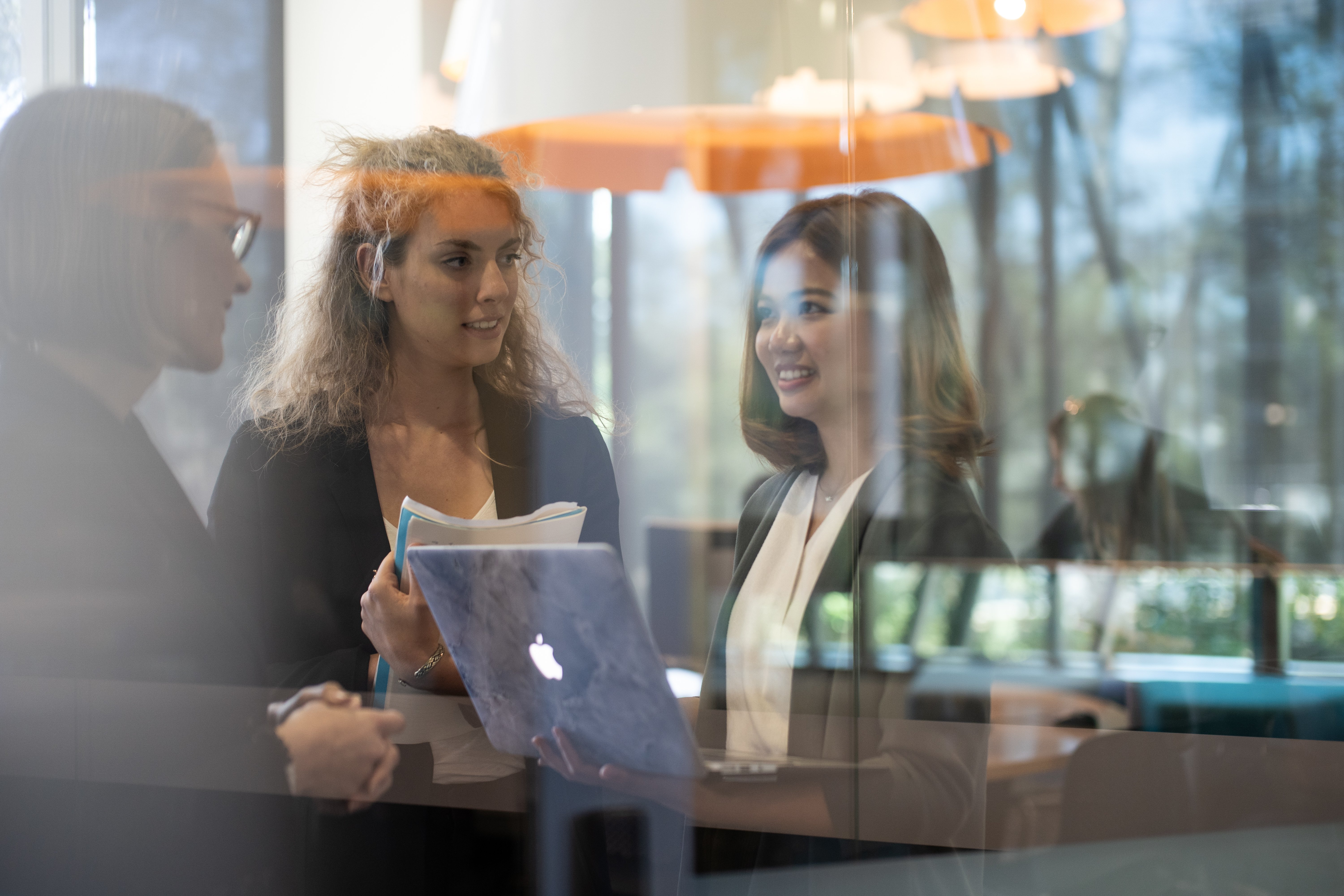 student speaking to teachers while holding laptop (as seen through glass wall)