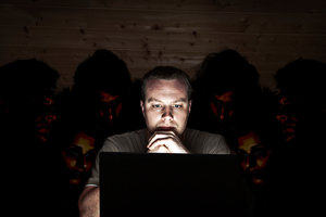 A cyber security threat - a man looks at his laptop, while people snoop over his shoulder
