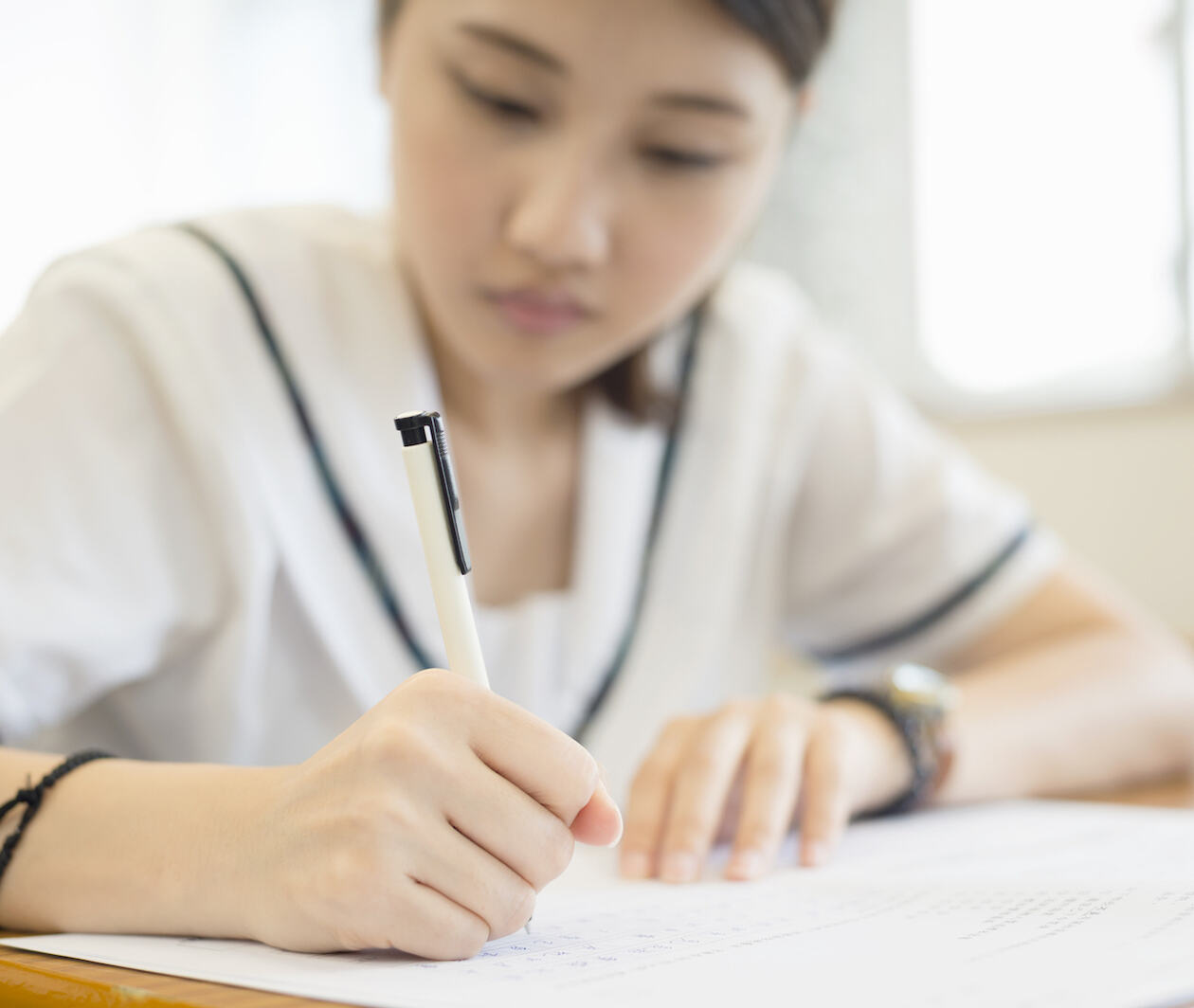 A Chinese student writing on an exam paper, hand holding pen in focus in the foreground