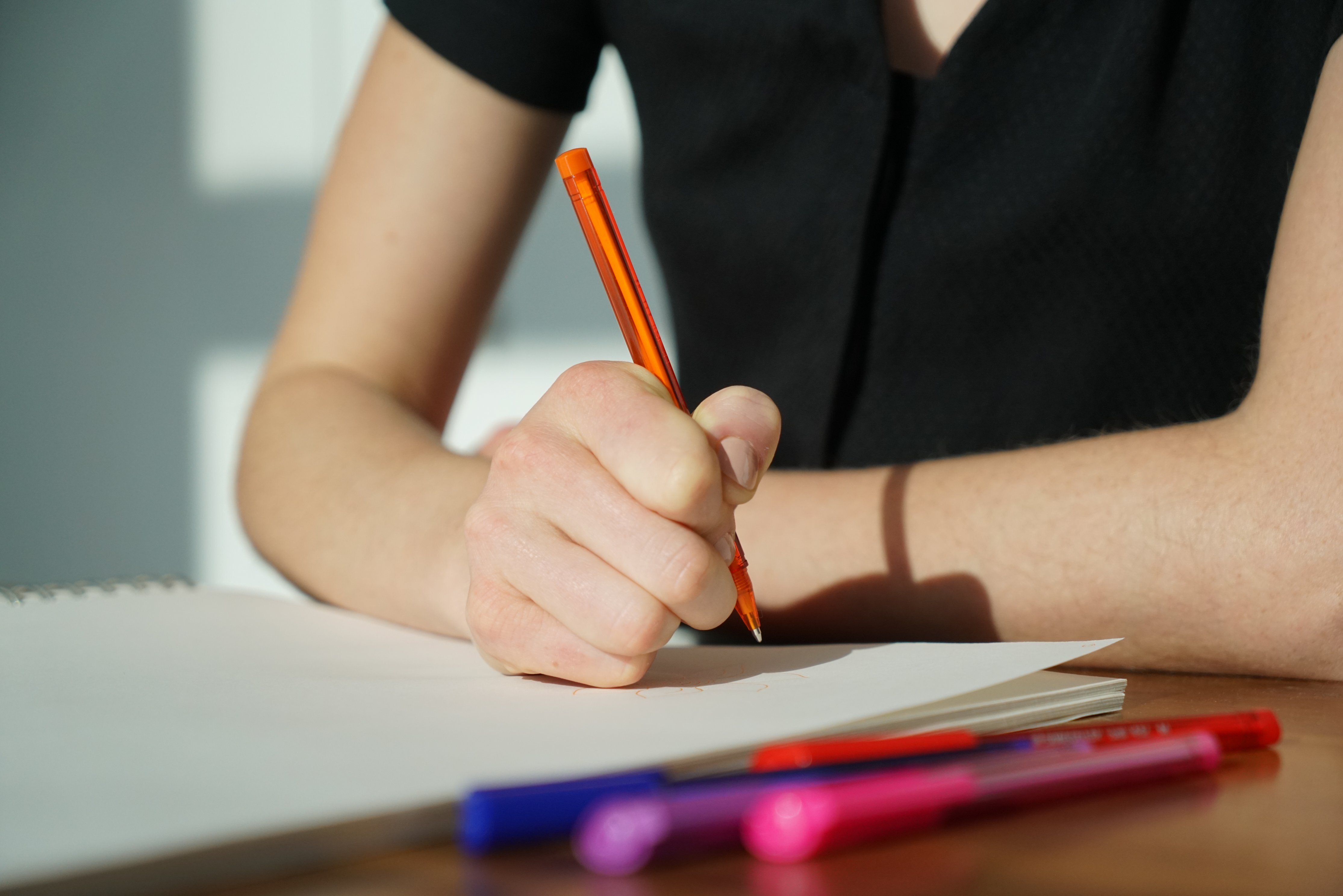 Student writing in a notebook with an orange pen.