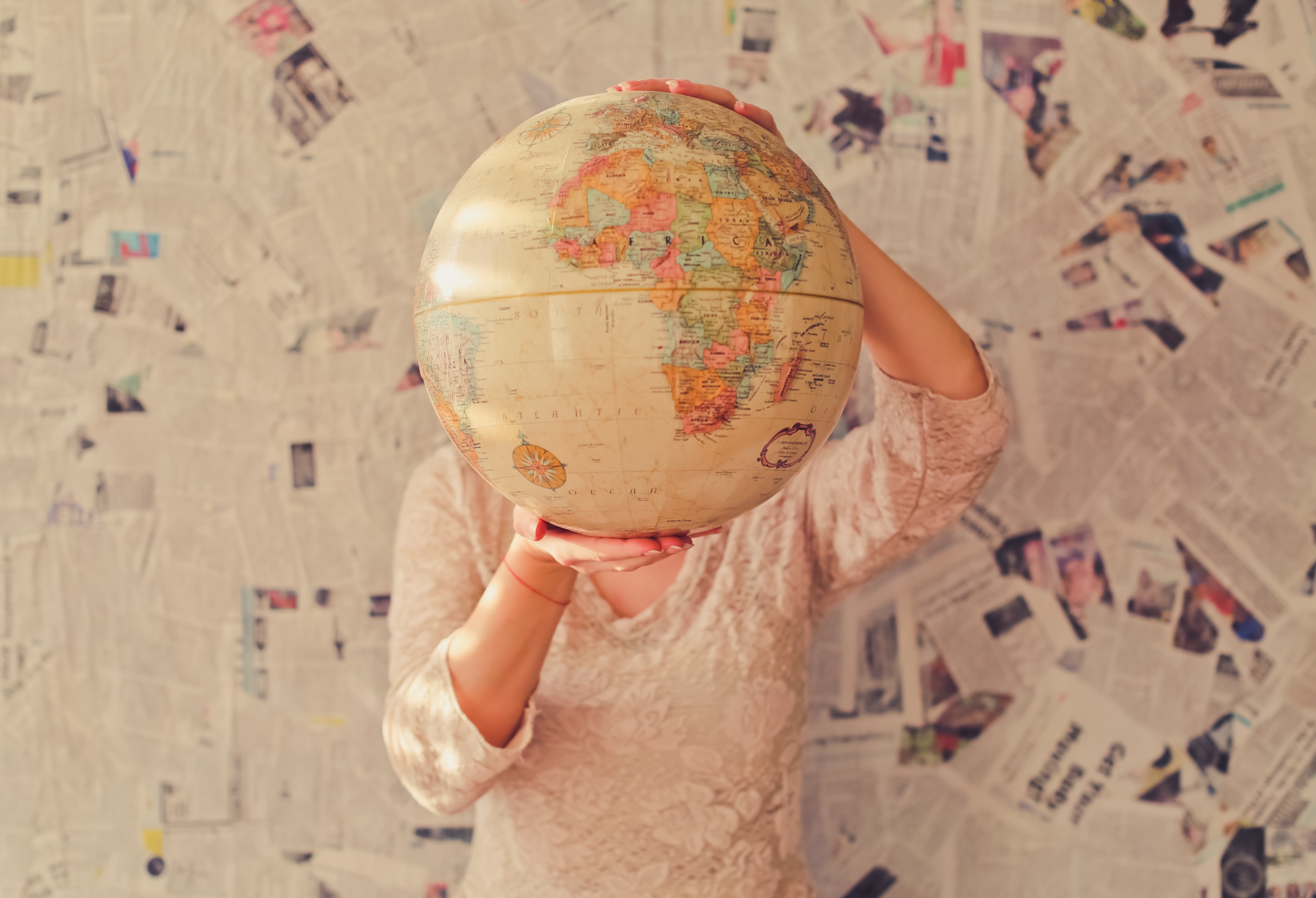 A woman holds a globe against a background of newspaper cuttings.