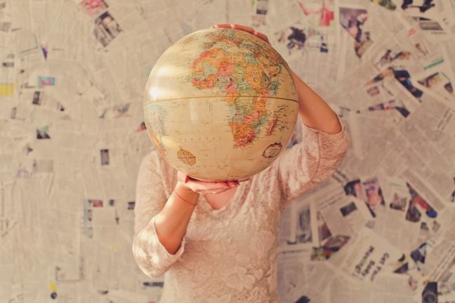 A woman holds a globe against a background of newspaper cuttings.