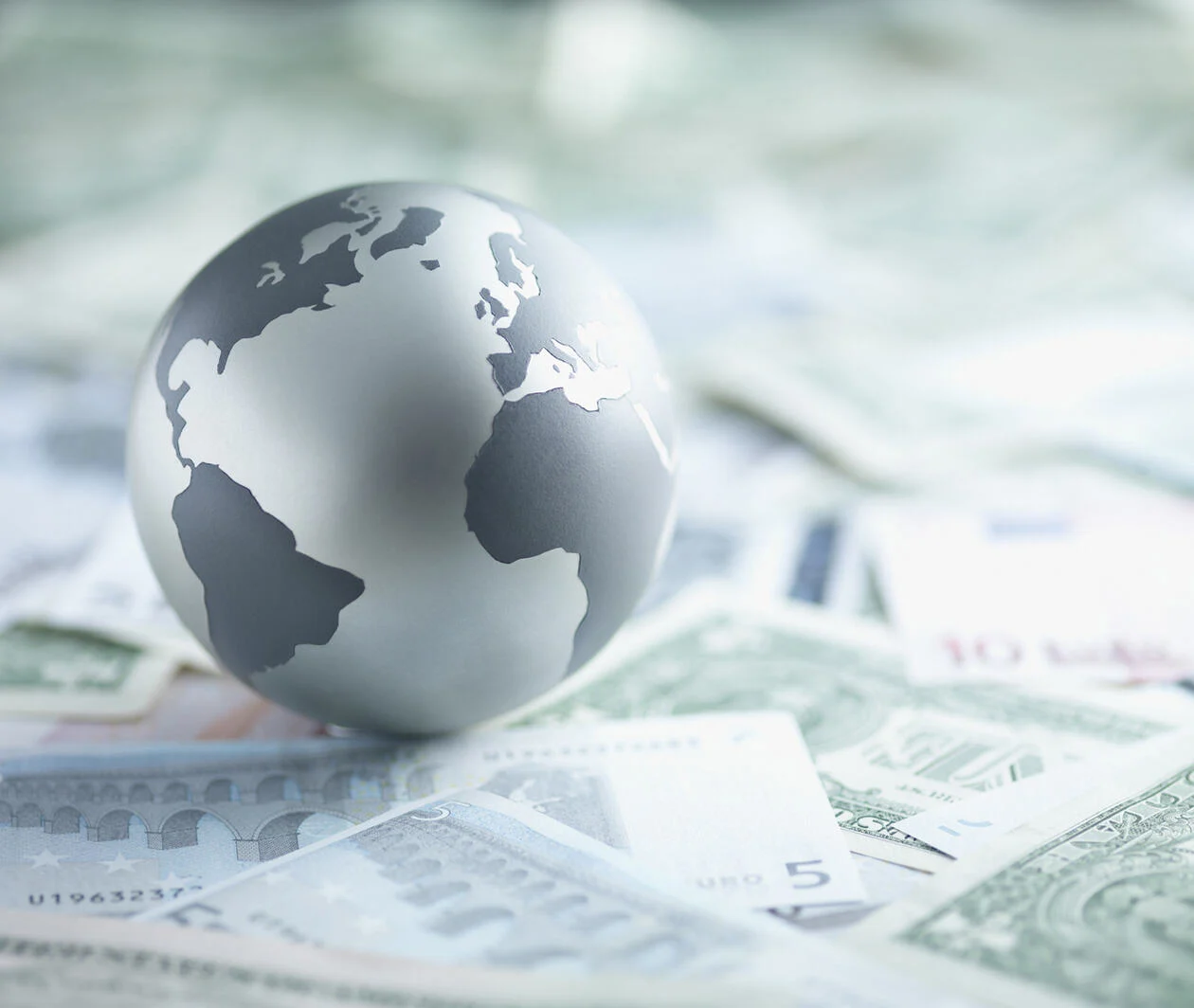 A metal globe resting on a pile of paper currencies including a 5 euro note.