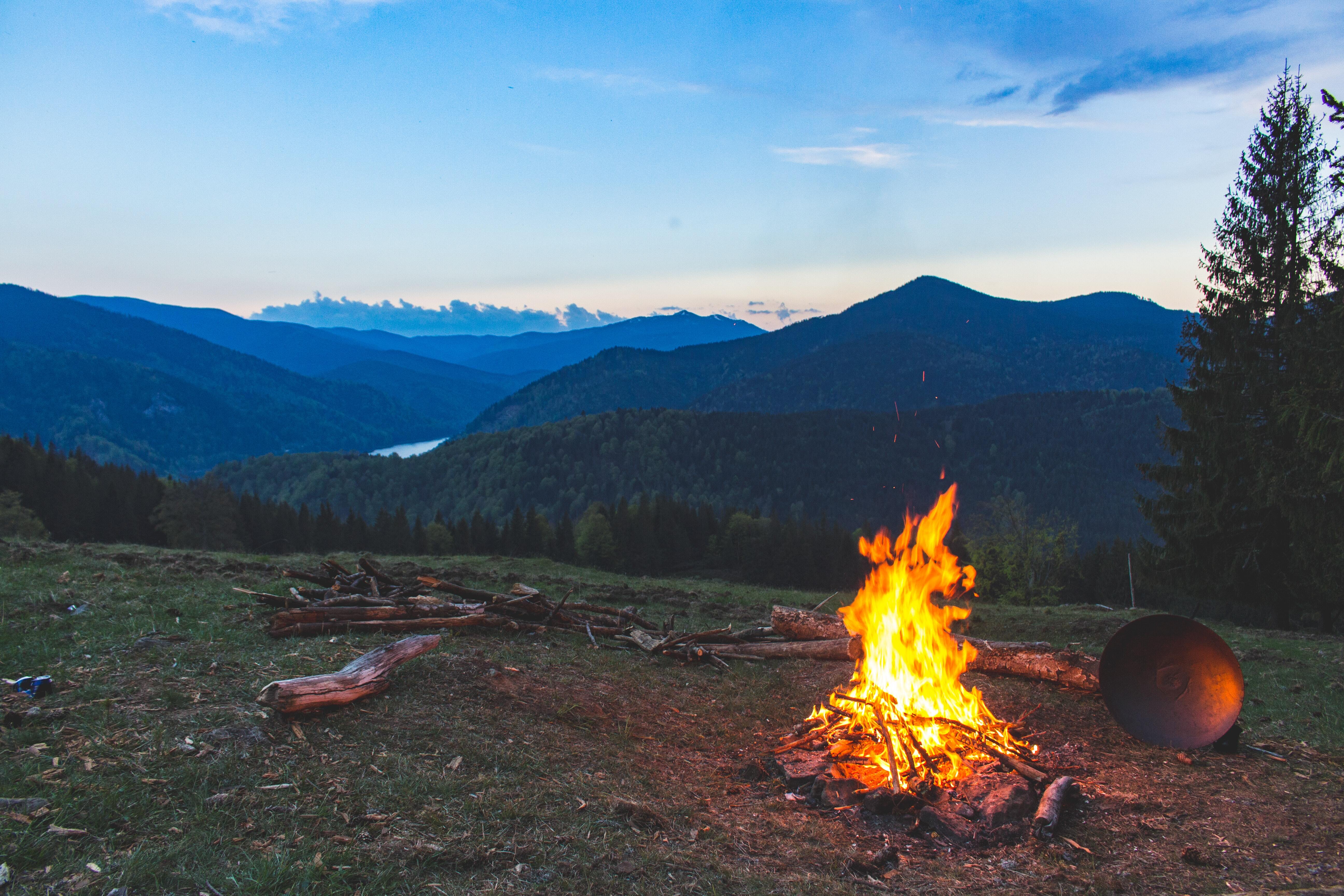 A campfire in the forest with blue skies and mountains in the background.