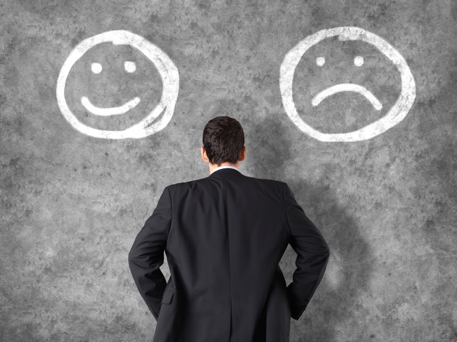 man facing a wall with a happy face on his left and a sad face on this write drawn on the wall