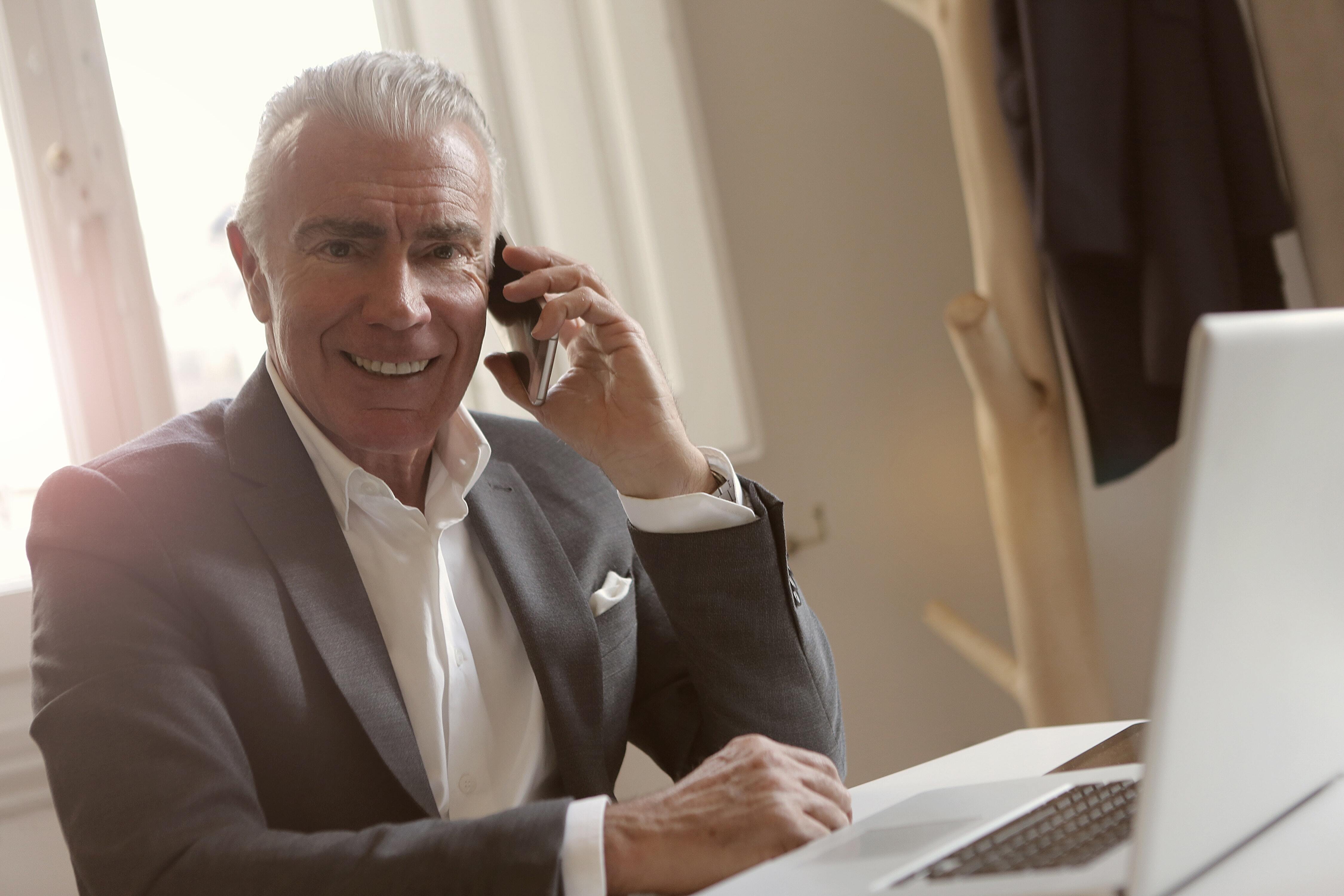 Man in a suit, in front of a laptop, smiling on the phone