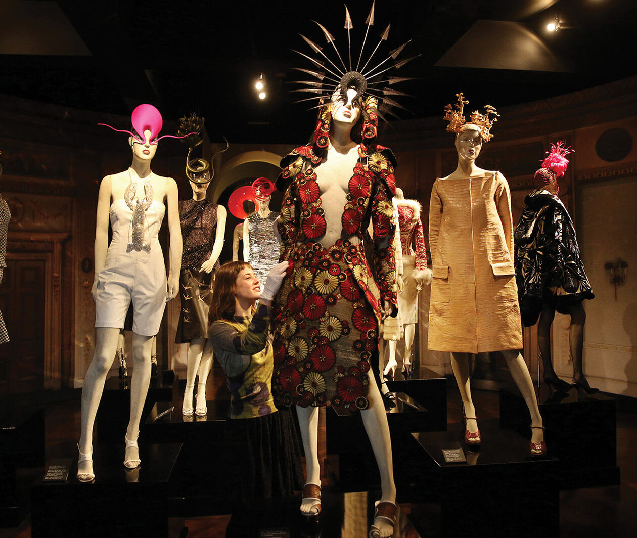 A woman styles a mannequin with a colourful patterned dress in a room full of styled mannequins.