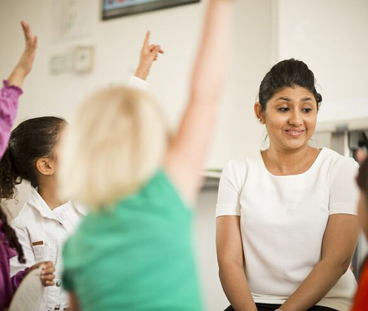 Teacher sitting among students with their hands raised