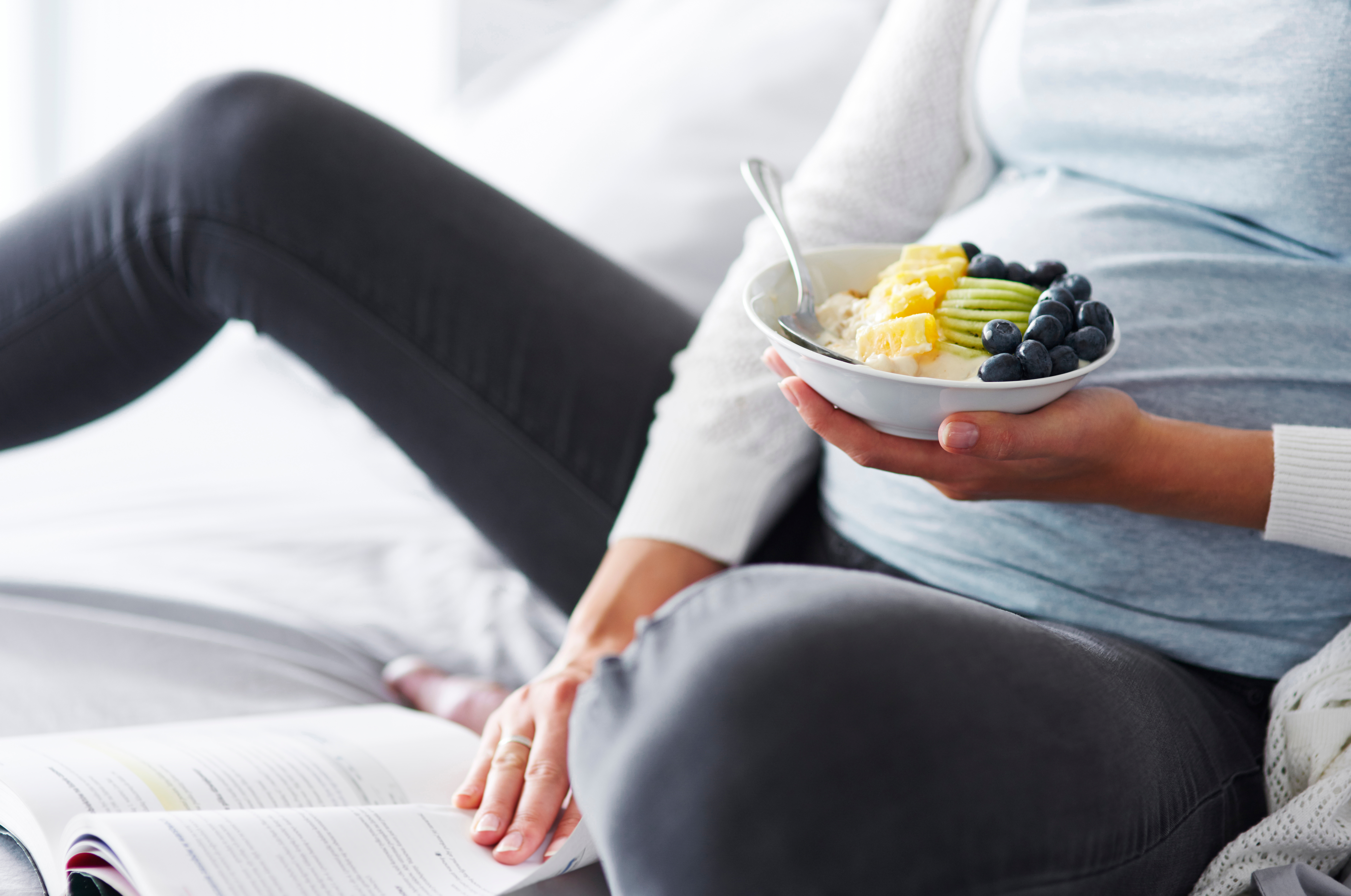 Pregnant woman reading and holding a bowl of fruit