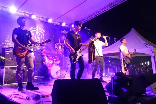 A band on stage, microphones and speakers can be seen